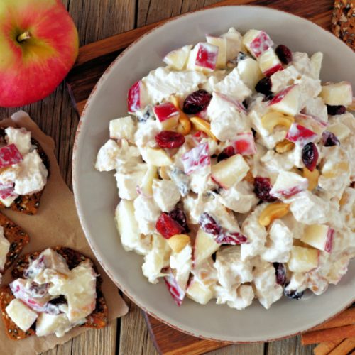 Cranberry chicken salad in a white bowl next to an apple on a counter