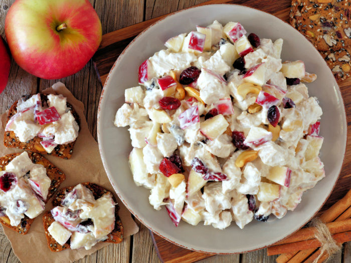 Cranberry chicken salad in a white bowl next to an apple on a counter