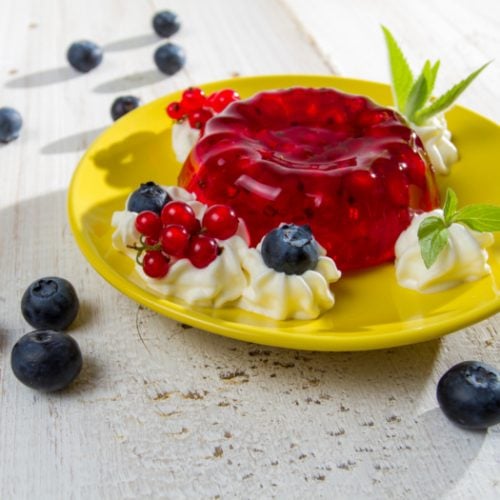 cranberry jello salad with whipped cream and berries on a yellow dish on a counter