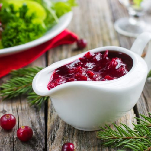 Cranberry sauce in a white serving bowl next to a dish on a wooden board
