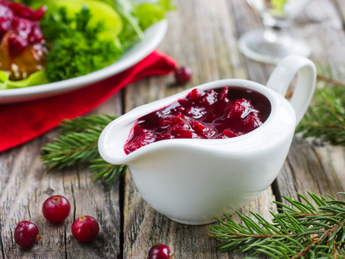 Cranberry sauce in a white serving bowl next to a dish on a wooden board