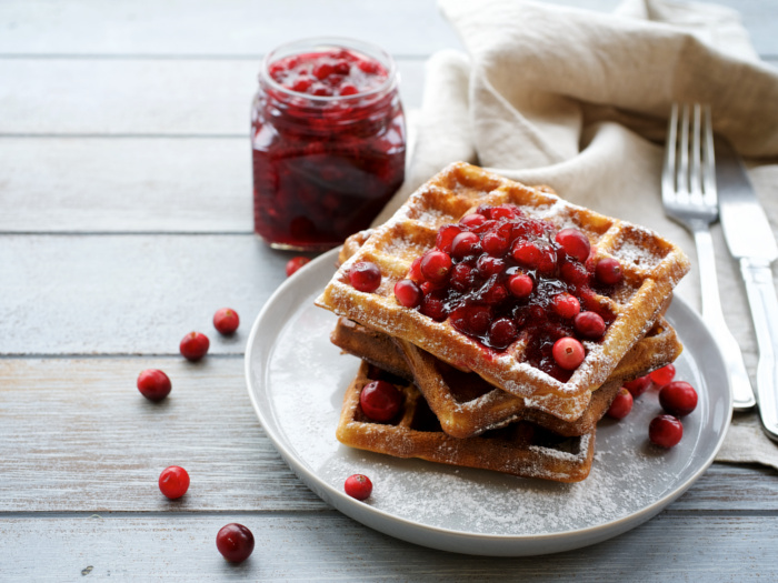 Waffles laden with cranberry sauce next to a jar filled with cranberry sauce, napkin, and fork