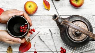 Cranberry tea in a cup and a kettle with two apples, a few leaves, and a tong