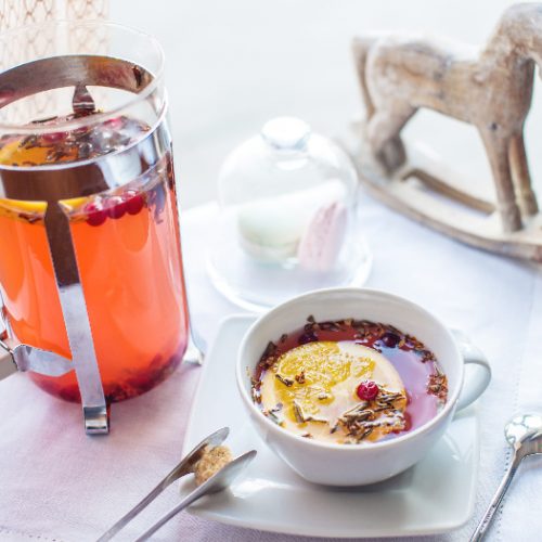 An image of a kettle and a cup of cranberry tea against a white background