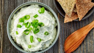 A flat lay picture of a bowl containing cream cheese next to a bowl of nachos