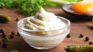 A bowl of homemade cream of tartar, pickles, parsley, dill, and mustard on a wooden table