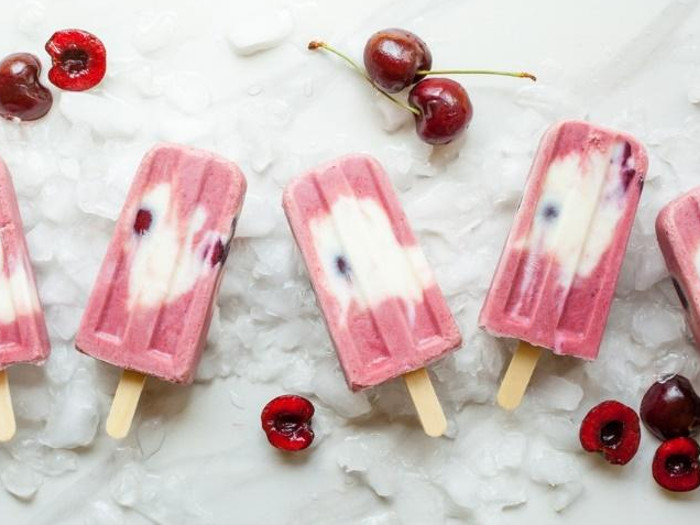 Creamy cherry popsicles on a plate with cherries beside