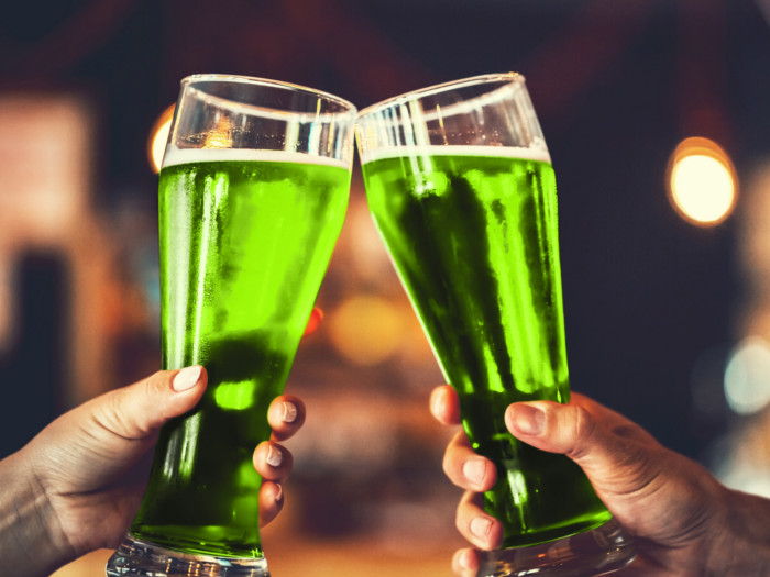 Two hands clinking glasses containing a green liquid.