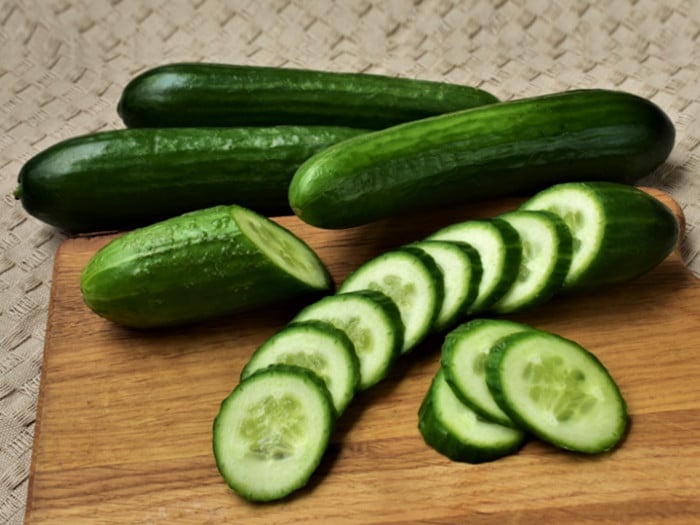 Fresh whole and sliced cucumber on a chopping board