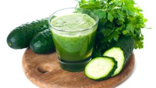 A glass filled with cucumber juice or smoothie surrounded with coriander, cucumbers and cucumber slices