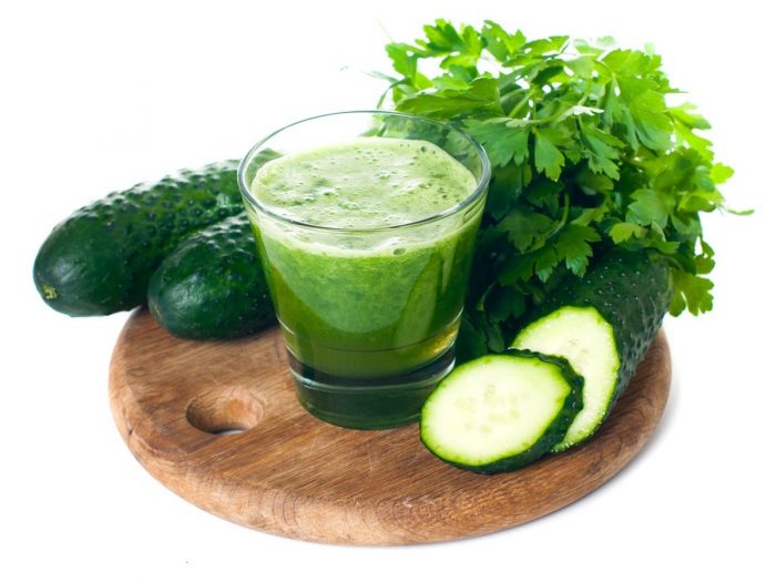 A glass filled with cucumber juice or smoothie surrounded with coriander, cucumbers and cucumber slices