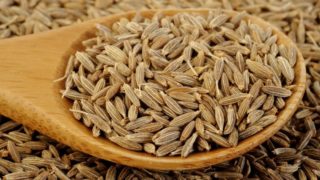 A close-up view of wooden spoon filled with cumin seeds