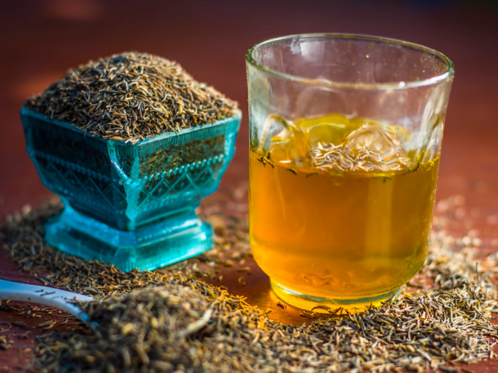 A glass of cumin water and a bowl of cumin seeds