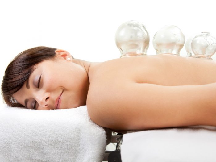 A woman lying on her stomach, smiling, with cups attached to her back