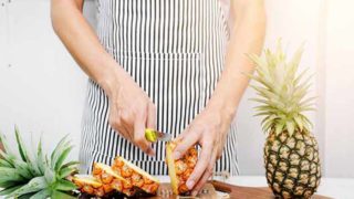 A woman with an apron slicing pineapple on a cutting board with a whole pineapple beside