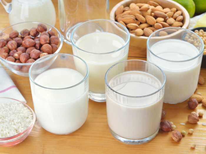 Four glasses of milk next to bowls full of almonds, chickpeas, and rice
