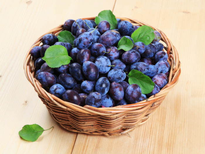 Close-up of damson plums with leaves in a basket