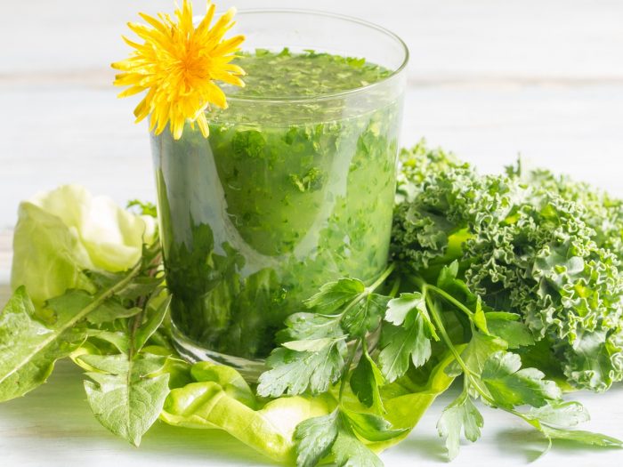 A glass of green juice topped with dandelion flower