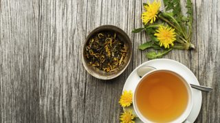 A cup of dandelion tea, some dandelion flowers and dried dandelion loose leaf tea on a table