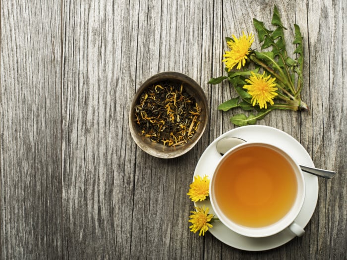 A cup of dandelion tea, some dandelion flowers and dried dandelion loose leaf tea on a table