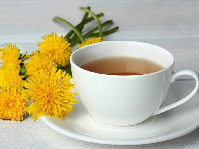 A cup of dandelion tea with flowers on a white table