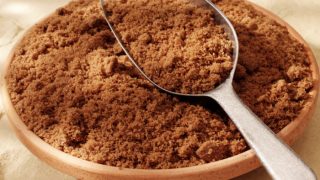 A wide bowl full of powdered brown sugar with a metal scoop