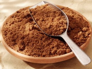 A wide bowl full of powdered brown sugar with a metal scoop