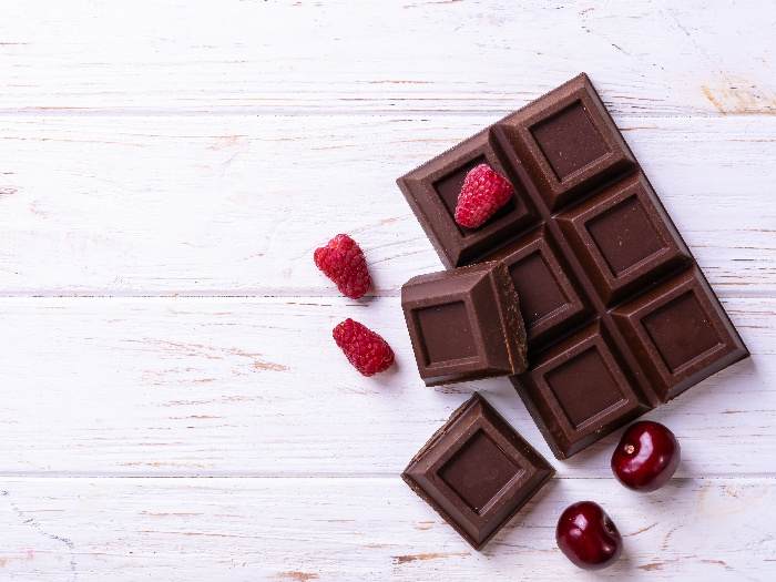 Broken chocolate bar slice with cherry and raspberry on white background