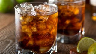Close-up of two glasses of dark liquor on the rocks with slices of lime