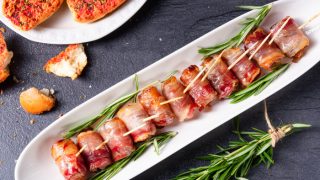 Bacon-wrapped dates served on a white tapas plate with rosemary