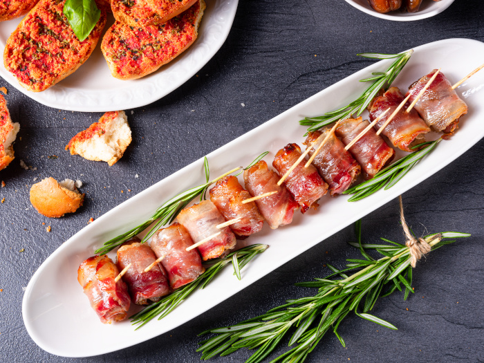 Bacon-wrapped dates served on a white tapas plate with rosemary