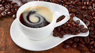A cup of steaming hot black coffee next to coffee beans