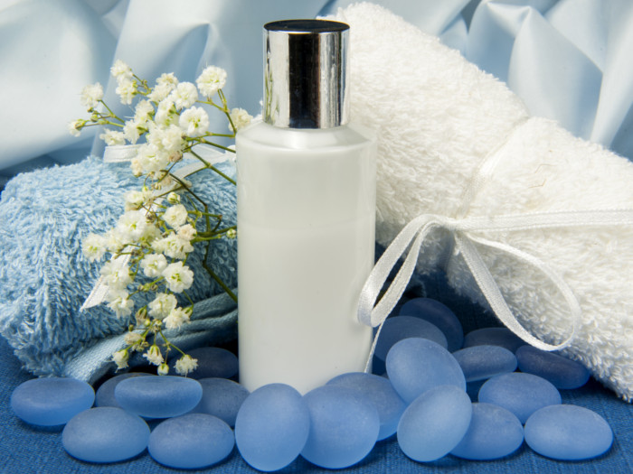 White bottle placed behind blue pebbles with white and blue towels placed at the back