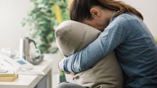 Girl with depressed posture stooping and hiding her face in a pillow.