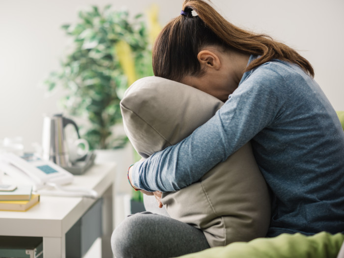 Girl with depressed posture stooping and hiding her face in a pillow.