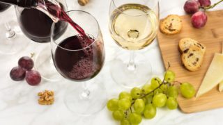 Glasses of red and white wine with grapes and cheese on the cutting board