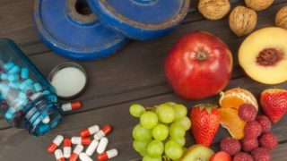 Fruits, nuts, a bottle of pills and weights placed on a wooden surface.