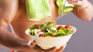 Close-up of a salad bowl and a fork held by a fit man in gym clothes