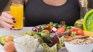 Close-up of a table full of healthy food with a woman holding a glass of juice at the back.