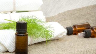 Dill oil with dill leaves on folded white towels in the background