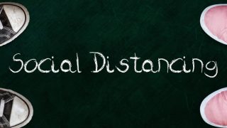 Two people standing on chalkboard with the word social distancing in between.