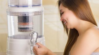 Woman taking distilled water in a glass from a water filter