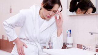 A pregnant woman sitting on a couch holding her head and looking stressed