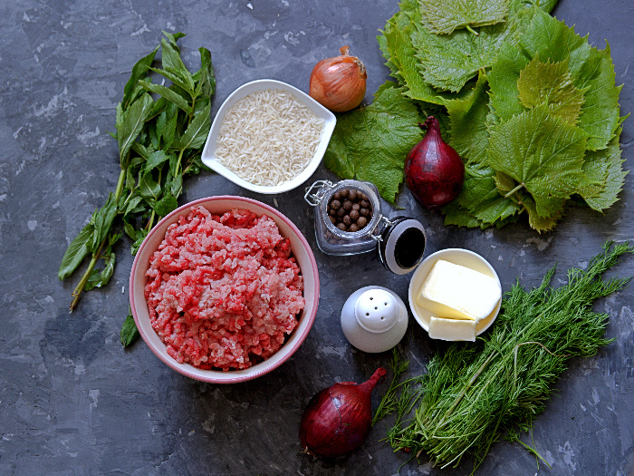 Ingredients for cooking dolma (minced meat, fresh grape leaves, butter, rice, mint, onion, dill, spices)