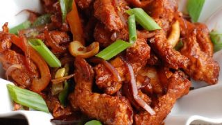 A close up shot of dragon chicken cooked with spring onion and cashews.