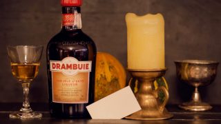 A bottle of Drambuie next to a glass filled with it and a candle