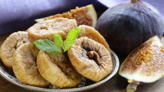 A plate of dried figs as well as whole and halved fresh mission figs on a wooden table