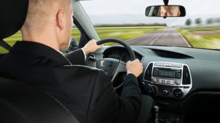 adult male driving a car on an empty road