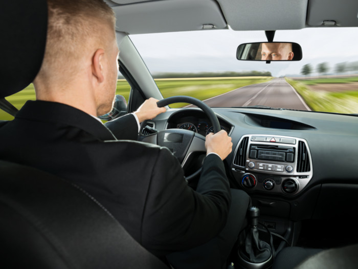 adult male driving a car on an empty road