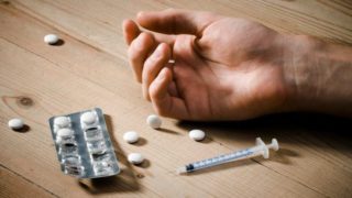 Hand of a drug addict with syringe and pills lying on a wooden floor